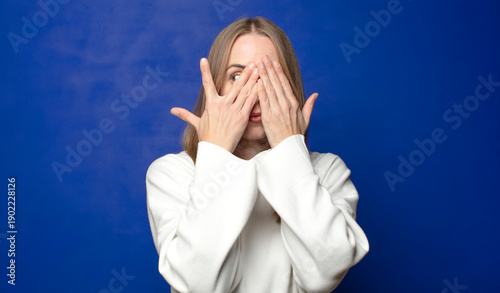 covering face with hands, peeking between fingers with surprised expression and looking to the side