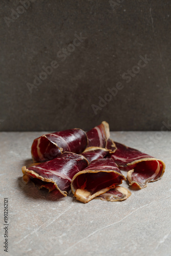 Elegant curls of Spanish cured beef cecina presented on a dark stone surface in a sophisticated low-light setting. Premium artisanal charcuterie with rich textures and deep tones, evoking luxury dinin