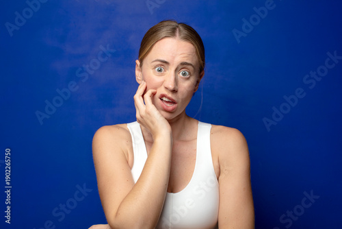 Quadro su tela blonde woman open-mouthed in shock and disbelief, with hand on cheek and arm cro