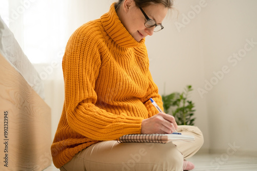 Expecting mother writing essential items list for maternity hospital in cozy home setting. Organized preparation for upcoming delivery and baby arrival.