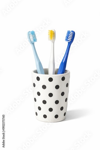Three colorful toothbrushes standing in polka dot cup on white background