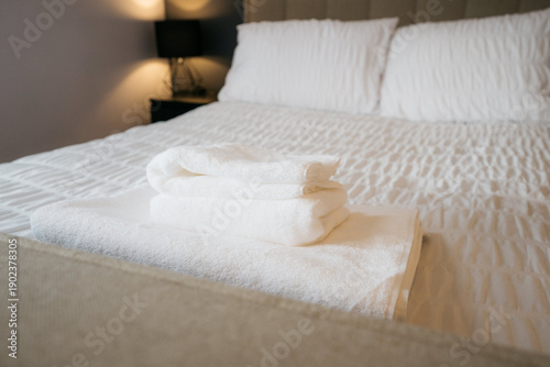A bed with white sheets and a stack of white towels on top of it