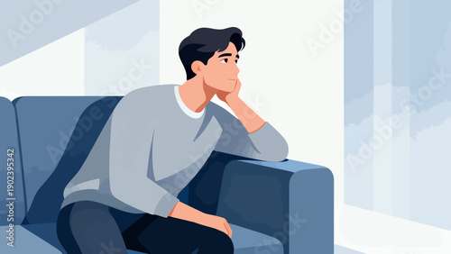 A man is sitting on a couch and looking down. He is sad or upset. The couch is blue and the room is well lit