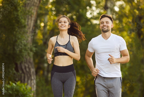 Foto Sporty fit active man and woman running together on sunny park path smiling, gre