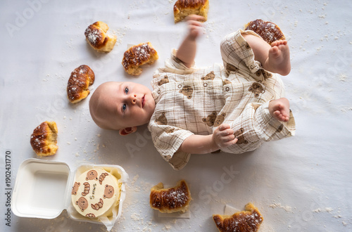 A baby is laying on a table with a bunch of donuts and a few pieces missing
