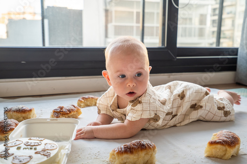 A baby is laying on the floor next to a box of donuts