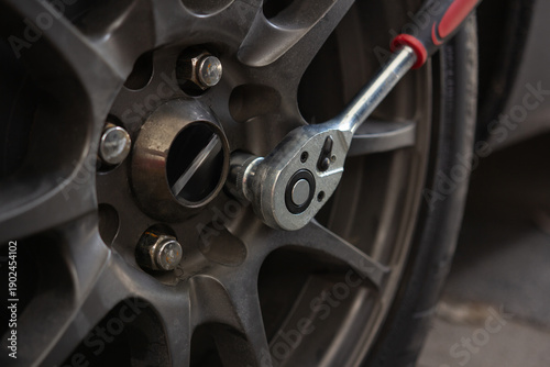 Bilde på lerret Close-up of a person loosening a car wheel lug nut with a hex socket wrench during automotive maintenance