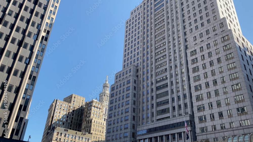 Obraz premium Modern and historical skyscrapers forming a dense urban canyon in the financial district of new york city, with office buildings reaching high into a bright blue sky