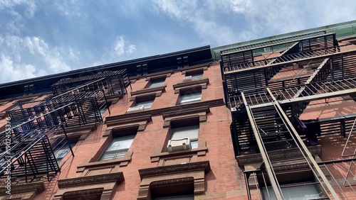 Historic new york city brownstone apartment building with exterior fire escapes and brick facade under a bright blue sky, symbolizing classic urban architecture