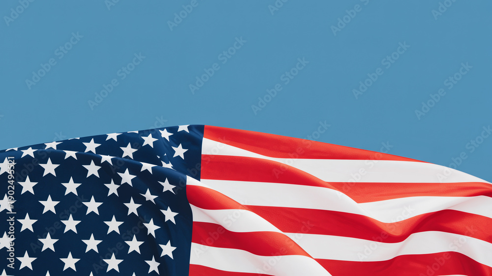 Obraz premium Patriotic American flag waving gracefully against a clear blue sky background representing national pride freedom and United States holiday celebrations like Fourth of July or Memorial Day