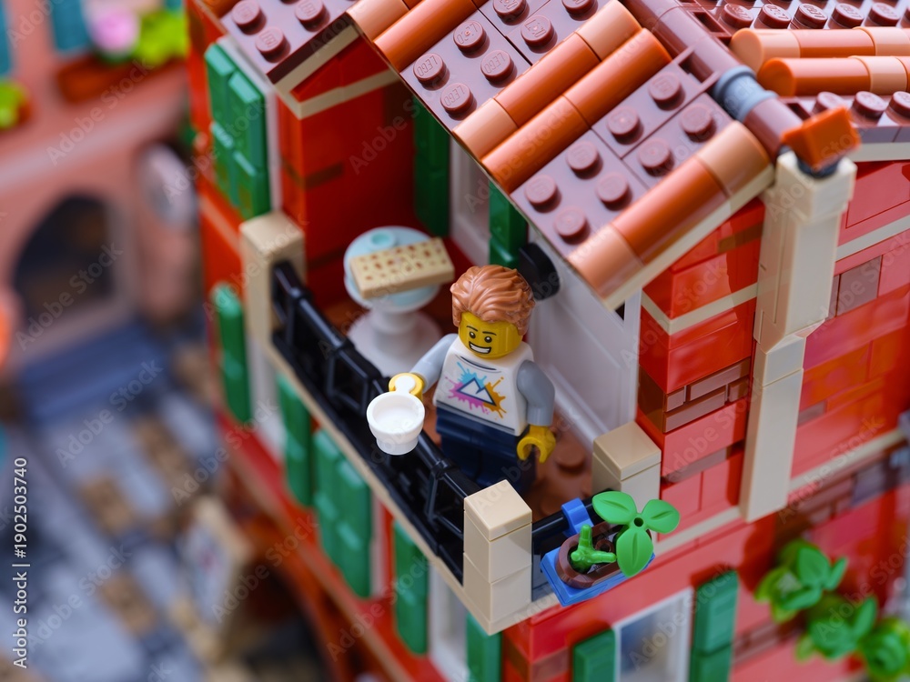 Obraz premium Tambov, Russian Federation - January 04, 2026 Lego man minifigure with white cup standing on a balcony in Mediterranean city.
