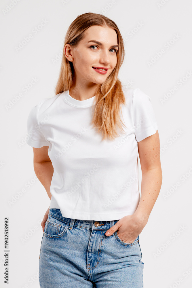 Obraz premium Smiling young woman posing in white t shirt and blue jeans for casual fashion concept