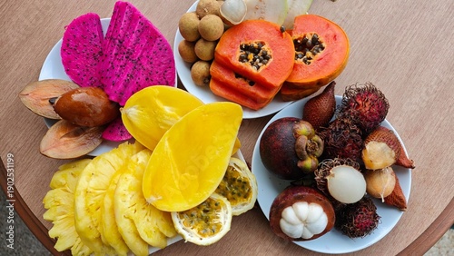 Assorted tropical fruits on white plates including dragon fruit, papaya, mango, rambutan, mangosteen, longan, and passion fruit