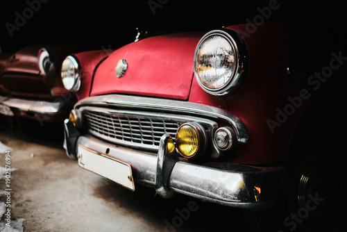 Close-up detail of red vintage car headlight with chrome bumper. Retro automotive design with dark background.