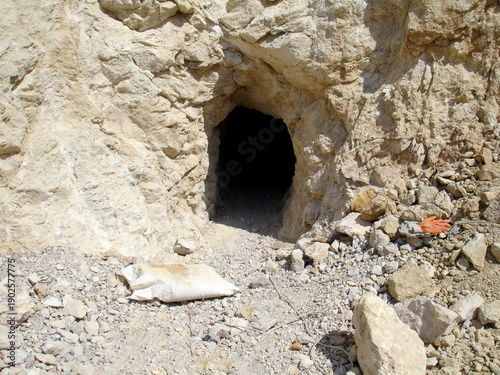 Close-up of a small, dark tunnel entrance hand-drilled into a limestone quarry wall. View of a narrow mine shaft opening surrounded by loose rocks and rubble in an industrial site.