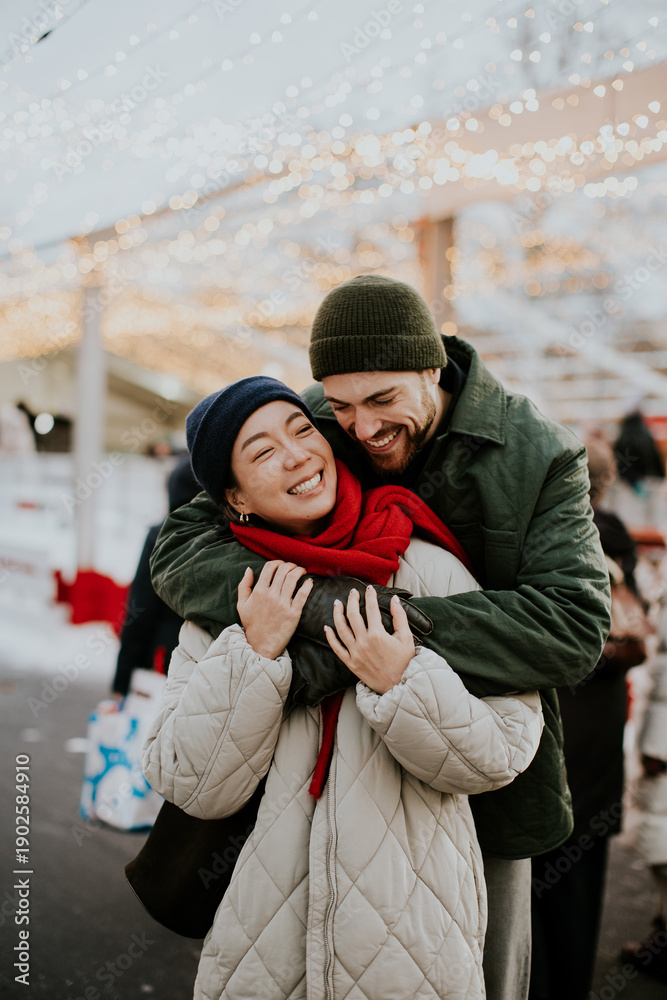 © BGStock72 - Couple enjoys winter fun in a festive outdoor market with holiday lights