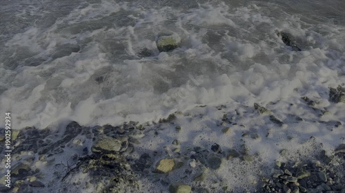 Slow motion 12fps of waves coming on shore with pebbles on beach and foam nature background UK 4K