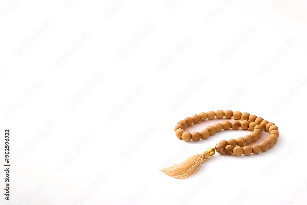 Obraz premium Wooden prayer beads with a tassel arranged on a minimalist white background.
