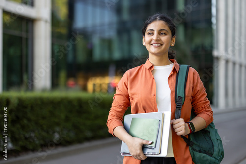 Cuadro en lienzo Young happy female student carrying a backpack and notebooks, smiling and lookin