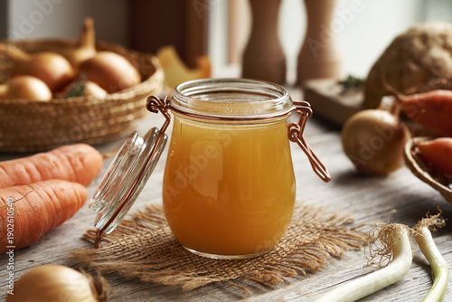 Chicken soup or bone broth in a glass jar on a wooden table
