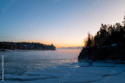 Photos Split Rock Lighthouse seen from a distance across the icy, vast expanse of Lake Superior, highlighting its isolation on the rugged North Shore cliffs