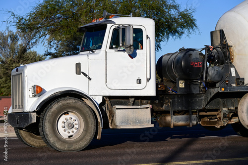 Φωτογραφία White concrete mixer truck driving on a paved road, representing commercial cons