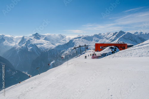 People enjoy skiing and snowboarding in Bad Gastein. The sun shines on the snow-covered slopes. Ski lifts take riders to the top of the mountain. Beautiful mountains surround the area.