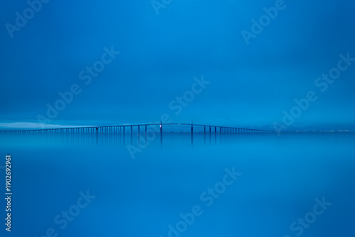 Sunshine Skyway Bridge captures the elegance of its sweeping cables beneath a textured, overcast sky. Soft clouds drift above while the structure stretches confidently across the horizon, creating a s