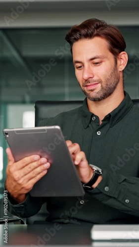 Smiling European 30s trade manager looking at digital tablet screen sitting at desk in office. Executive professional man working online using computer for financial business banking work. Vertical