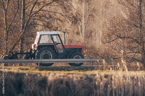 Agricultural Tractor Driving Along Rural Road in Autumn Landscape