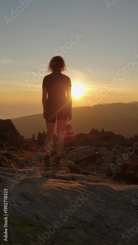 Adventurous Woman Enjoys Breathtaking Golden Sunset From Mountain Peak In North Vancouver, BC, Canada