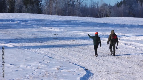 Two people walking together across a snow-covered field on a cold winter day, surrounded by frosty trees and soft blue light, with open copy space in the landscape.