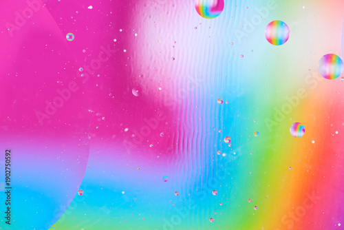 Artistic abstract liquid art with oil drops on pink, blue and green blurred background.