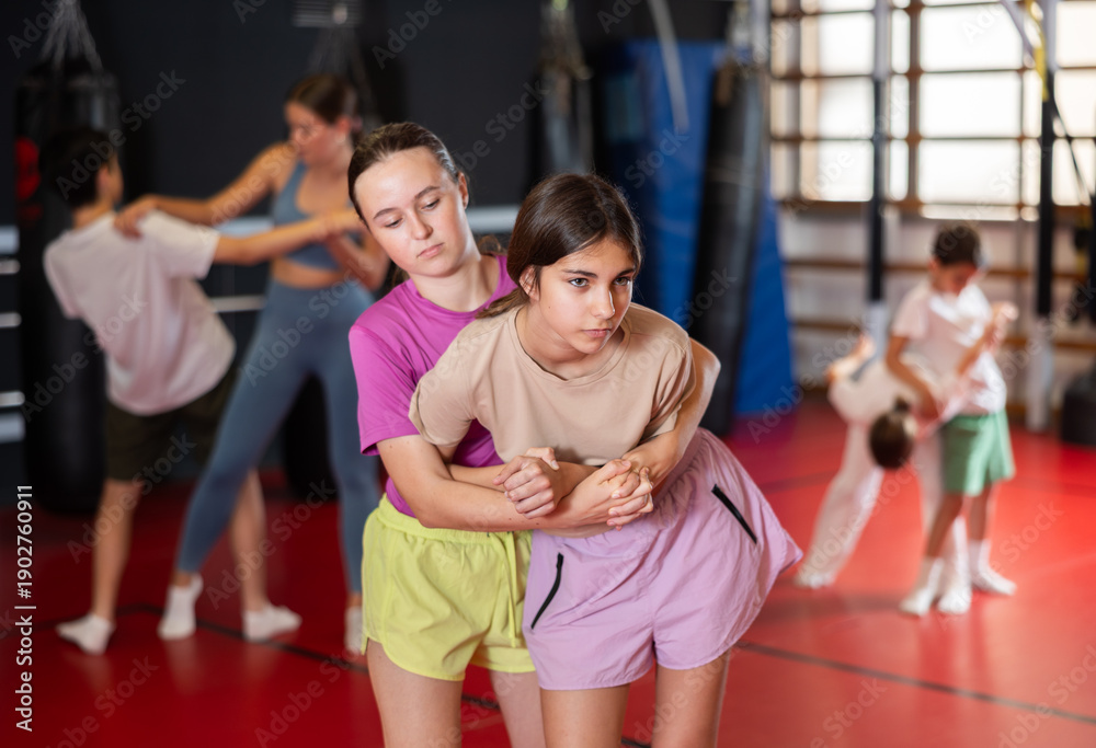 Fototapeta premium Teen girls train in pairs to strike and reflect blows of enemy. Self-defense training and Krav Maga principles, physical activity, sports self-defense classes...