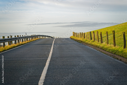 Slika na platnu New blacktop road rising with fence and posts under blue sky.