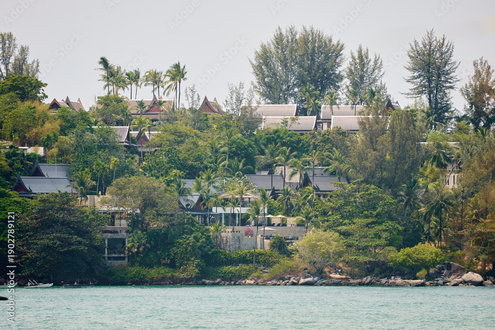 Obraz premium Thailand's coast on a sunny day, villas and hotels among palm trees on a hill, people on a jet ski, a yacht off the coast