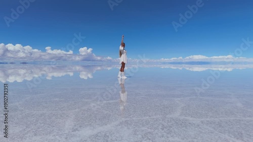 A woman points at the sky and walks on the expansive Salar de Uyuni salt flats in Bolivia, under a clear blue sky