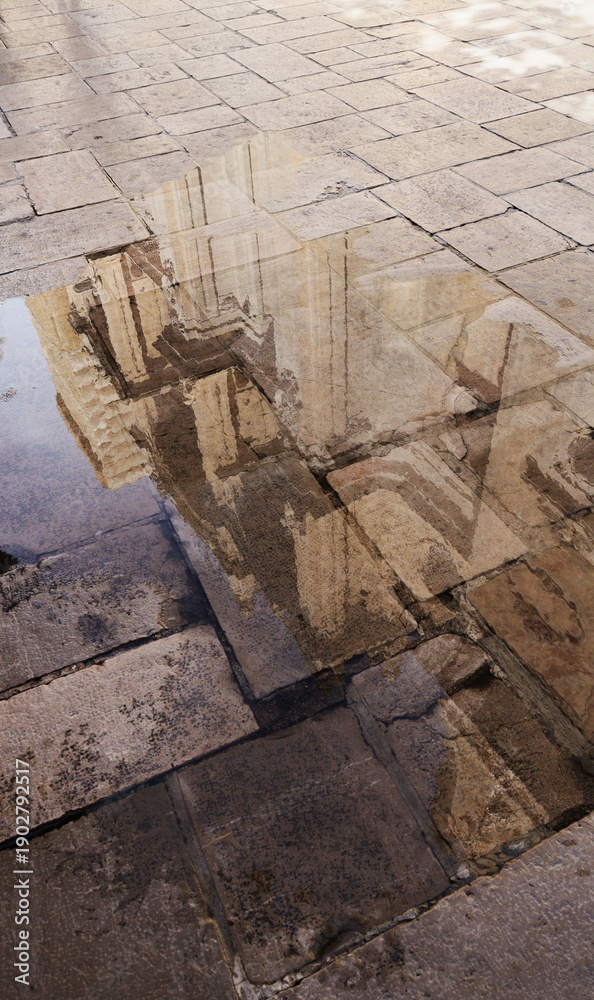 Obraz premium Reflection of a church facade in a puddle on old cobblestone pavement on a sunny day.