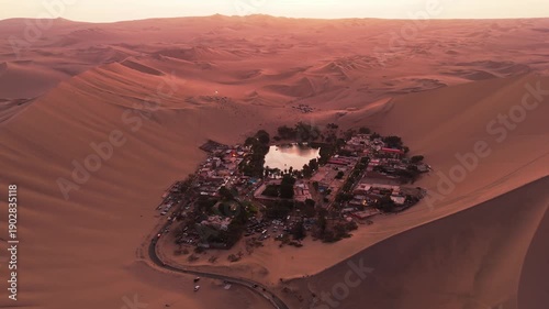 Aerial view of Huacachina oasis in Peru, showcasing sand dunes and a tranquil lake at sunset