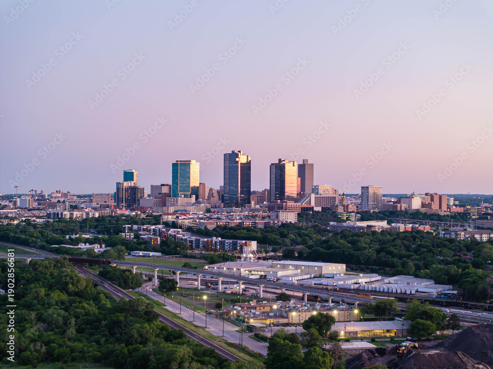 Fototapeta premium Aerial view of Fort Worth, Texas at dusk, vibrant cityscape, prominent skyscrapers, modern low residential buildings, active rail yard, and lush greenery