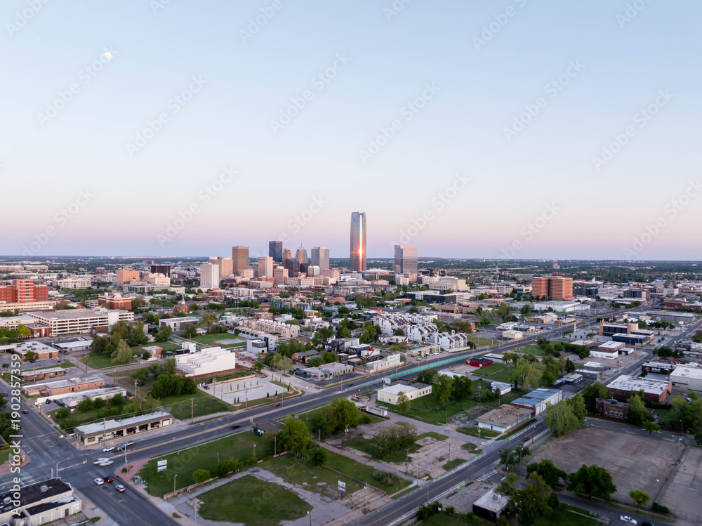 Fototapeta premium Aerial view of Oklahoma City skyline, including Devon Energy Center, glowing in the sunset with the moon overhead, highlighting urban growth and city infrastructure