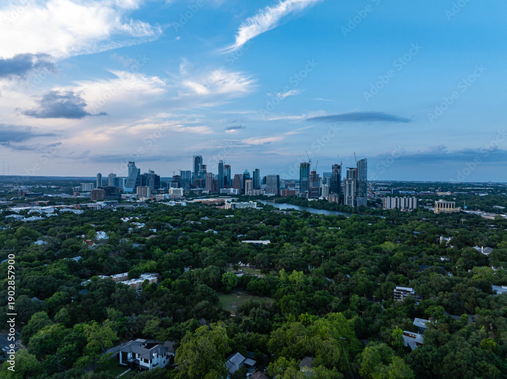Obraz premium Austin, Texas skyline stands tall above lush greenery at dusk, showcasing coexistence of cityscape and nature under a partly cloudy sky