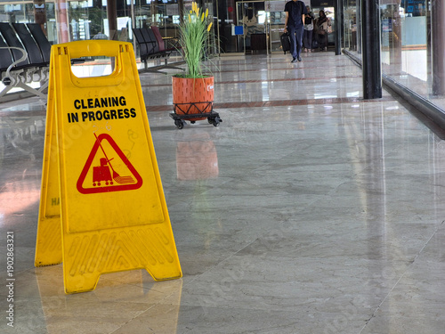 Minimal interior scene showing a yellow Cleaning in Progress caution sign placed on a marble tile floor, photographed from above with ample copy space and soft indoor lighting.