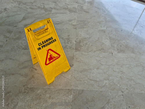 Minimal interior scene showing a yellow Cleaning in Progress caution sign placed on a marble tile floor, photographed from above with ample copy space and soft indoor lighting.