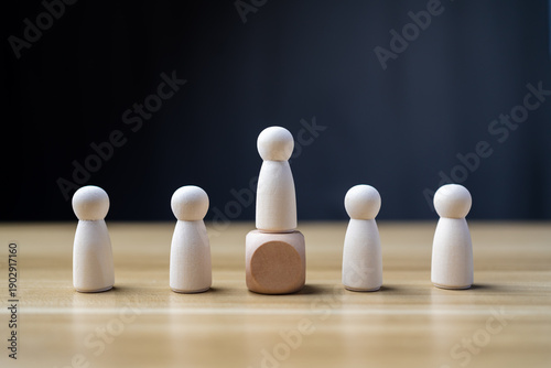 Foto Leadership concept with one tall wooden peg doll standing on block above group