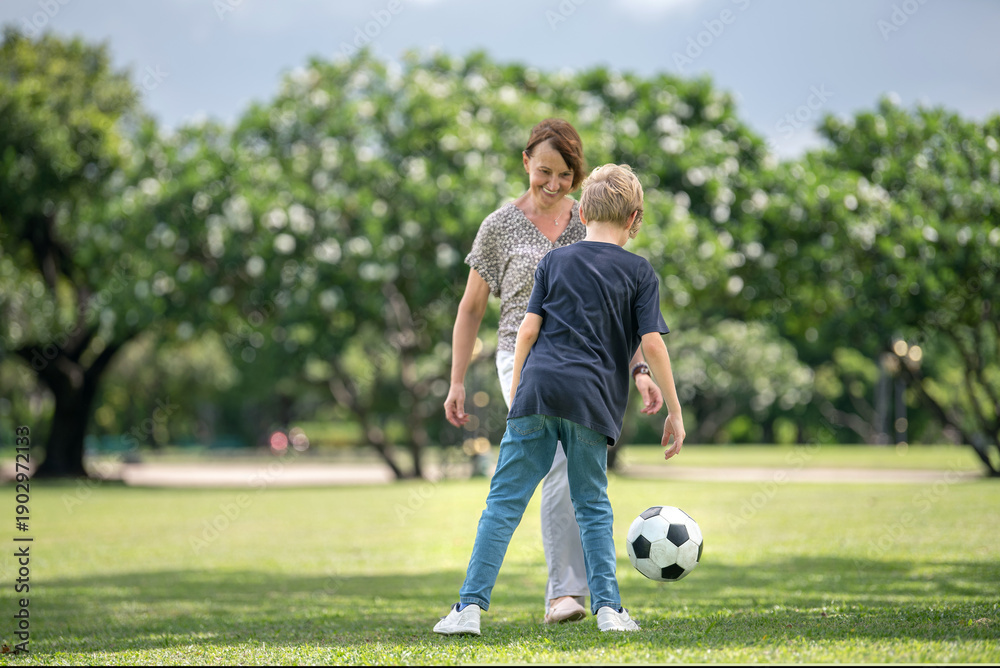 Obraz premium grandmother and grandson bonding joyful family moment playing soccer together. Happiness grandparent and childhood on weekend with football outdoor activity emotional connection
