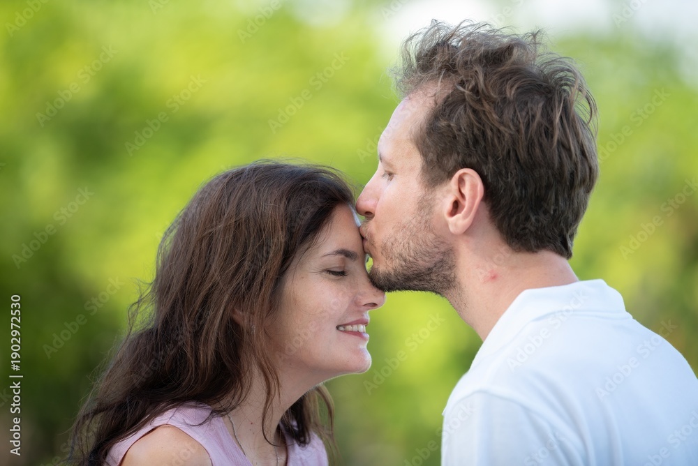 Obraz premium Affectionate man kissing woman forehead tender emotional love and trust between couple peaceful romantic gesture in outdoors. Happy couple sharing gentle intimate moment in garden.