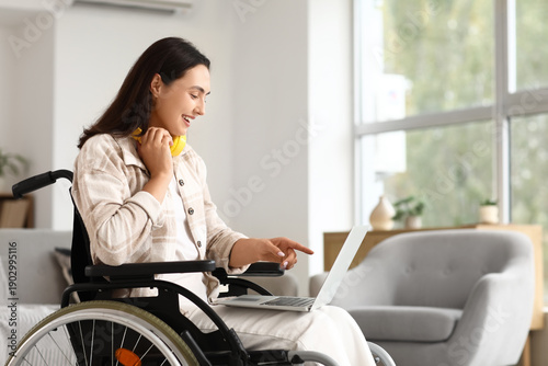Young woman in wheelchair using laptop at home