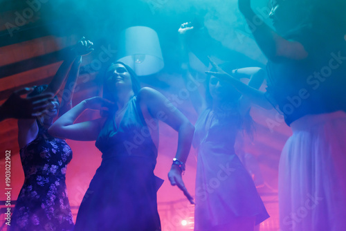 Obraz na plátně Group of young women dancing at a party under colorful lights and misty atmosphe