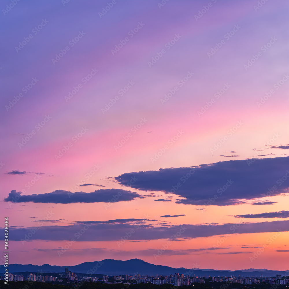 Obraz premium Breathtaking sunset sky with pink and purple hues over a distant city skyline and mountain range.